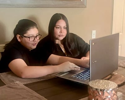 Two people sitting at a table looking at an Acer laptop screen together, both wearing dark clothing.