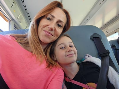 A person with reddish hair wearing a pink top sitting next to a child on what appears to be a bus or vehicle with blue seats visible.