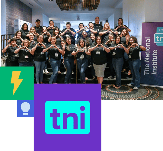 A group photo of approximately 20-25 people at a Carnegie Learning The National Institutes conference.. They're arranged in rows and are making heart shapes with their hands in a coordinated pose. Everyone is wearing matching dark t-shirts, suggesting they belong to the same organization or team. The bottom of the image features a logo with 'tni' in purple, a lightning bolt icon in yellow, and a partial text that reads 'The National Institute.' The setting appears to be an indoor venue with modern décor..
