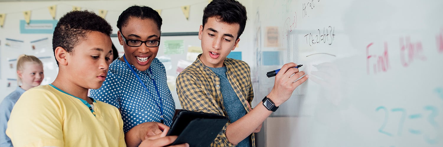 Two middle school students work at a whiteboard with their teacher.
