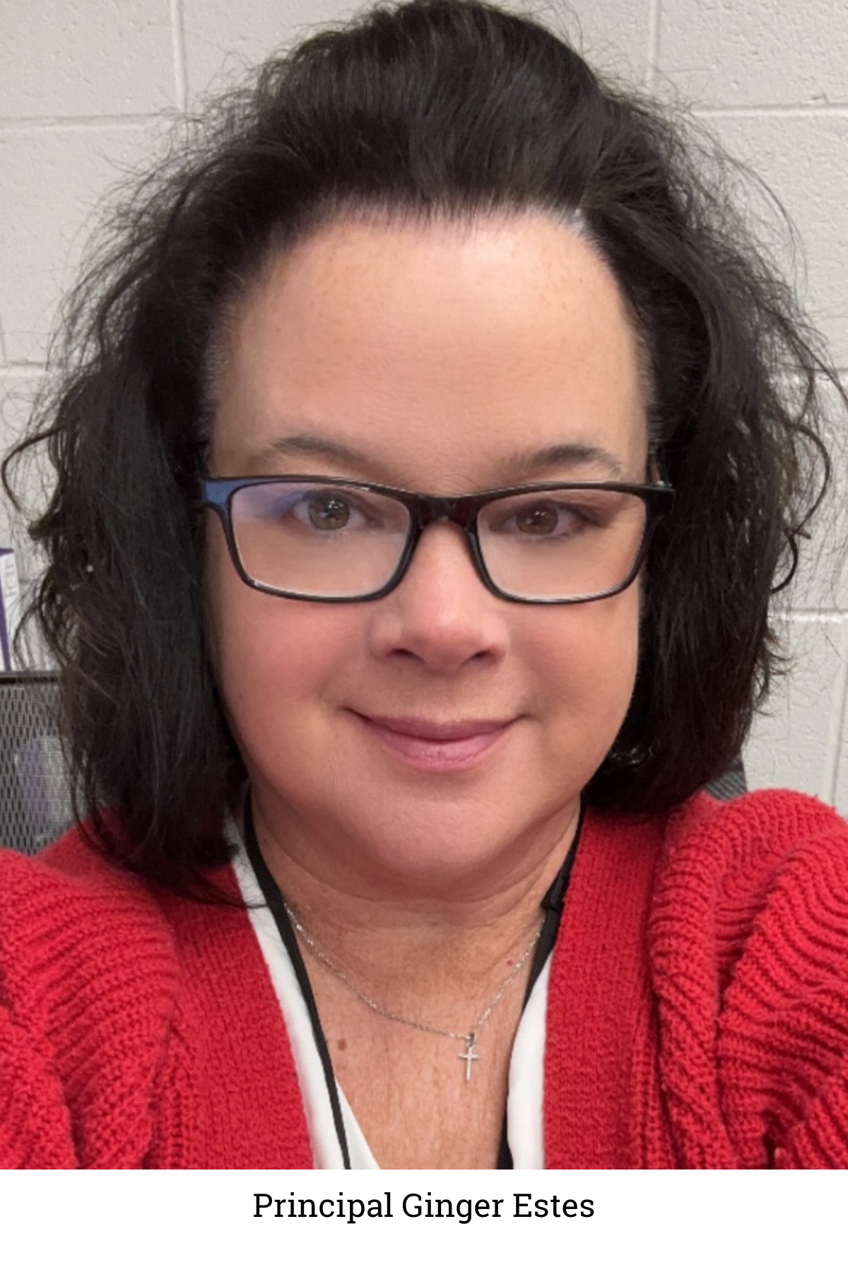 Ginger Estes smiles into the camera wearing a red sweater, black reading glasses and white shirt.